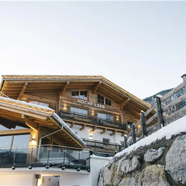 A cozy wooden mountain house with a balcony and a beautiful view. The surroundings are characterized by snow and mountains.