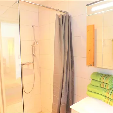 Ein modernes Badezimmer mit einer Dusche aus Glas und einem großen Spiegel. Auf der Ablage liegen bunt gefaltete Handtücher in verschiedenen Farben.
