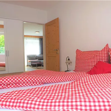 Ein gemütliches Schlafzimmer mit einem Doppelbett und rot-weiß karierter Bettwäsche. Im Raum gibt es einen Kleiderschrank und viel Tageslicht.
