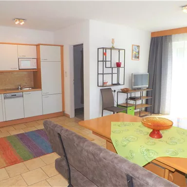 Eine moderne Wohnung mit offener Küche und einem gemütlichen Wohnbereich. Der Raum ist hell und freundlich, mit buntem Teppich und einem Esstisch.