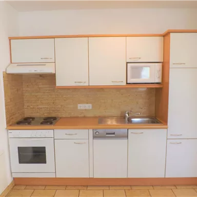 Eine moderne Küche mit weißen Schränken und einer hellen Arbeitsplatte. Sie verfügt über einen Herd, einen Kühlschrank und eine Spüle.