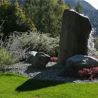 A beautiful garden with a large stone and colorful flowers. Green lawns and bushes surround the stones.