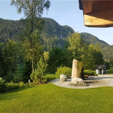 A tranquil landscape with green meadows and high mountains in the background. Rock formations and trees create a harmonious atmosphere.