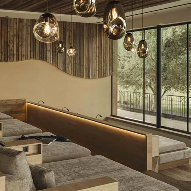 Ein modernes Entspannungszimmer mit bequemen Liegen und Holzdetails. Große Fenster bieten einen Blick auf die grüne Landschaft.