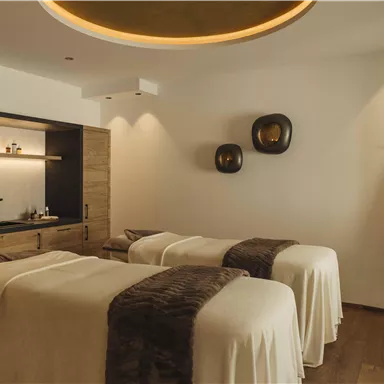 Ein stilvolles Spa mit zwei Behandlungsliegen und warmem Licht. An der Wand befinden sich dekorative Elemente und ein Regal mit Pflegeprodukten.