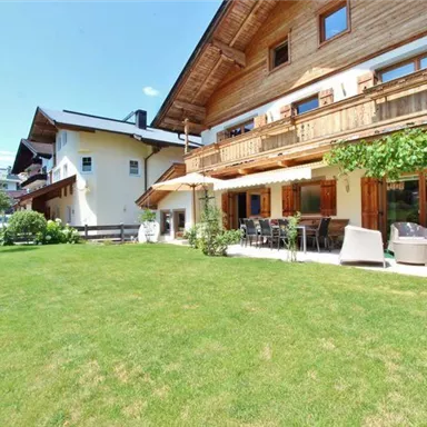 Ein schönes Haus mit Holzverkleidung und mehreren Balkonen. Der Garten ist grün und einladend mit Sitzgelegenheiten im Freien.