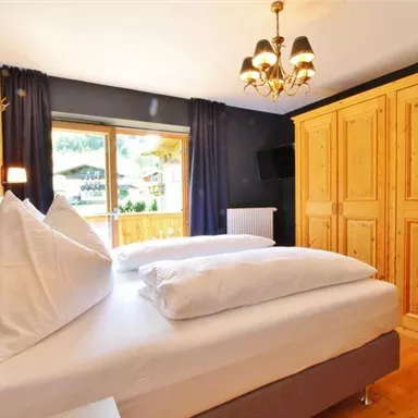 Ein modernes Schlafzimmer mit zwei Betten und einer Holzkommode. Das Fenster bietet einen Blick auf die Außenumgebung und lässt viel Tageslicht herein.