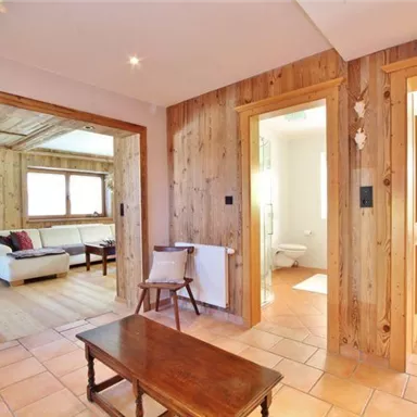 Ein einladender Flur mit Holzwänden und Terrakottaboden. Links befindet sich ein gemütlicher Wohnbereich mit einem Sofa.