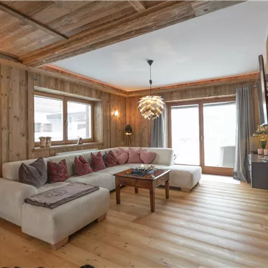 Ein gemütliches Wohnzimmer mit Holzverkleidung und großen Fenstern. Ein einladendes Sofa und ein moderner Couchtisch schaffen eine behagliche Atmosphäre.