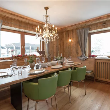 Ein gemütlicher Essbereich mit Holzwänden und einem eleganten Kronleuchter. Der Tisch ist gedeckt und bietet Platz für mehrere Gäste.