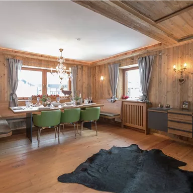 Ein gemütlicher Essbereich mit Holzverkleidung und einem großen Tisch. Grüne Stühle und eine elegante Lampe sorgen für eine einladende Atmosphäre.