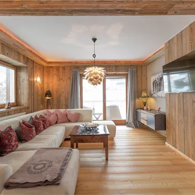 Ein gemütliches Wohnzimmer mit Holzwänden und einem großen, bequemen Sofa. Der Raum ist gut beleuchtet und hat eine moderne TV-Einheit sowie eine angenehme Atmosphäre.