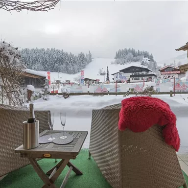 Eine gemütliche Terrasse mit zwei Stühlen und einem Glaseis in der Einsamkeit des Winters. Im Hintergrund sieht man schneebedeckte Hügel und eine malerische Berglandschaft.