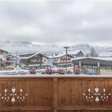 Ein malerischer Blick auf ein verschneites Dorf mit traditionellen Holzhäusern. Die Berge sind in Wolken gehüllt und schaffen eine gemütliche Atmosphäre.