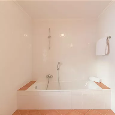 Ein helles Badezimmer mit einer Badewanne und warmen Fliesen. Die Wände sind weiß gefliest, und ein Handtuch hängt an der Wand.