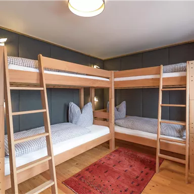 Ein gemütlicher Raum mit einem Etagenbett aus Holz und zwei Matratzen. Der Boden ist aus Holz und ein roter Teppich sorgt für zusätzliche Gemütlichkeit.