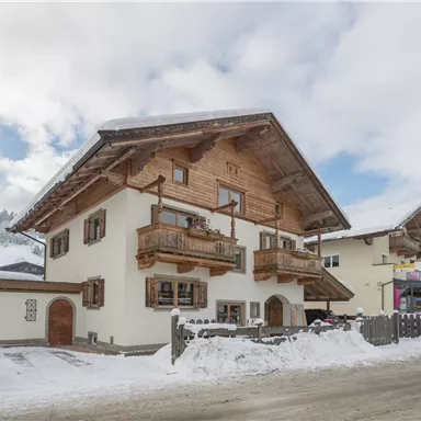 Ein gemütliches Holzhaus im Schnee mit Balkonen. Die umliegenden Berge sind leicht bewölkt und verleihen der Szene eine winterliche Atmosphäre.