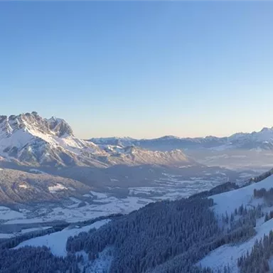 A breathtaking winter landscape with snow-covered mountains and a clear blue sky. In the foreground, a cable car is visible, leading into the mountains.
