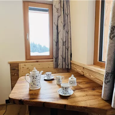 A cozy wooden table with a teapot and cups. Through the window, one can see a snowy landscape.