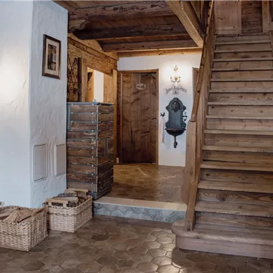 An inviting hallway with wooden paneling and a staircase. Basket organizers and wall lamps create a cozy atmosphere.