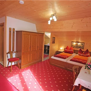 A cozy room with wood paneling and two beds. The room is comfortably furnished with a table, chairs, and a flower on the table.
