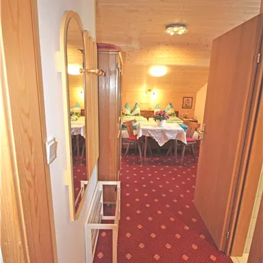 A hallway with wooden ceilings and carpet flooring. In the background, there is a table set with plates and decoration.