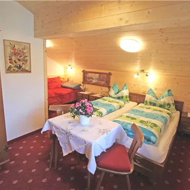 A cozy bedroom with two beds and traditional furniture. The room is brightly lit and decorated with a table and chairs.