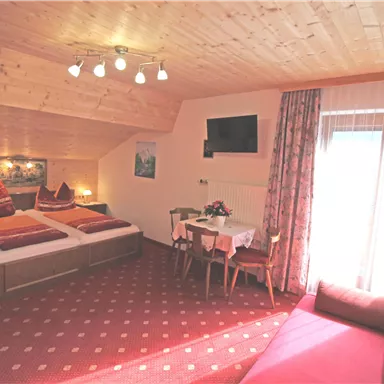 A cozy hotel room with wood paneling and a large bed. There is a television, a table, and a view of the balcony.
