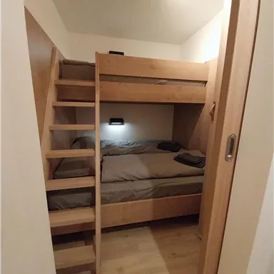 A cozy bedroom with a wooden bunk bed and a small staircase. The walls are light, and there is pleasant lighting.