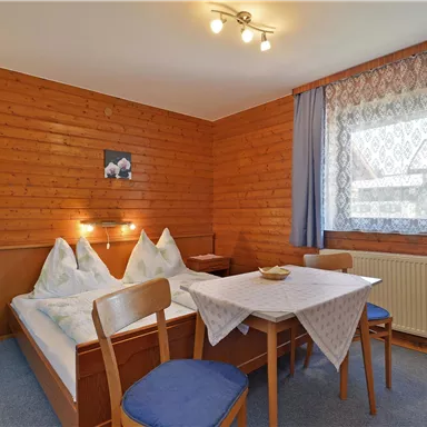 A cozy room with wood paneling, two beds, and a table. The window offers daylight and a view outside.