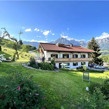 A beautiful house in nature with a well-maintained garden. In the background, mountains and a clear sky can be seen.