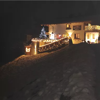 A beautifully lit house in the snow. Christmas lights and a decorated tree create a festive atmosphere.