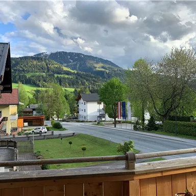 Eine malerische Landschaft mit grünen Hügeln und einer ruhigen Straße. Im Hintergrund sind Berge und Wolken zu sehen.