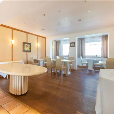 Ein modernes Restaurant mit hellen Wänden und einem großen runden Tisch. Die Sitze sind gemütlich und sorgen für eine einladende Atmosphäre.