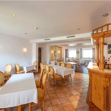 Ein helles Restaurant mit runden Tischen und Holzstühlen. Die Einrichtung ist einfach und einladend, mit großen Fenstern, die für viel Licht sorgen.