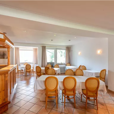 Ein helles Restaurant mit Holzdekor und runden Tischen. Die Stühle sind elegant und der Raum hat große Fenster für viel Tageslicht.