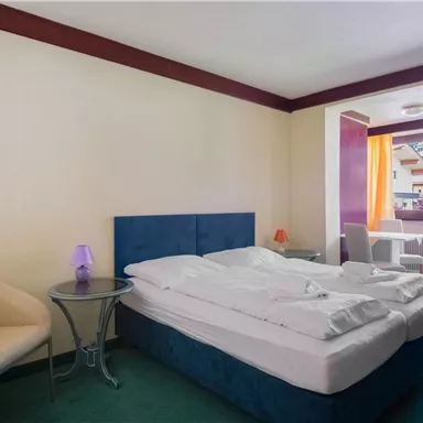 Ein gemütliches Hotelzimmer mit zwei Betten und einem kleinen Tisch. Große Fenster mit Blick nach draußen sorgen für viel Tageslicht.