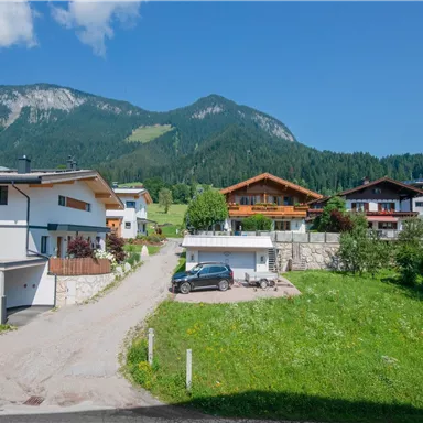 Eine malerische Wohngegend mit modernen Häusern und einer grünen Wiese. Im Hintergrund sind beeindruckende Berge und ein blauer Himmel zu sehen.