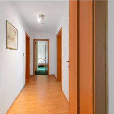 Ein heller Flur mit Holzböden und orangefarbenen Türen. Im Hintergrund sind zwei weitere Räume sichtbar.