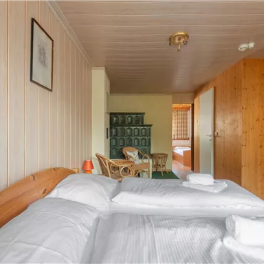 Ein gemütliches Zimmer mit zwei Betten und wohltuendem Holzinterieur. Im Hintergrund sind ein Schrank und ein Tisch mit Stühlen sichtbar.