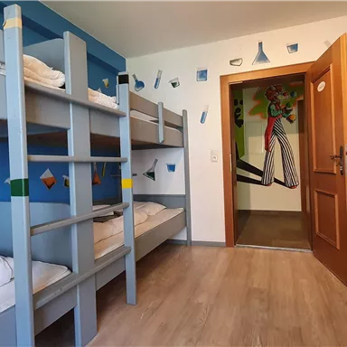 A friendly dormitory with bunk beds and colorful walls. The door leads to another room.