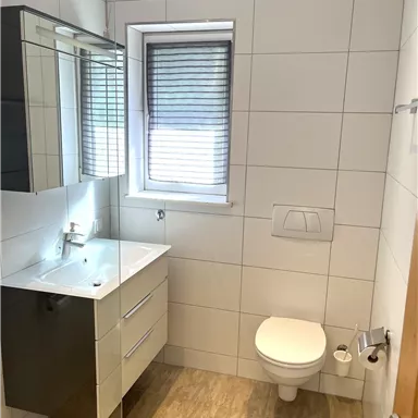 A modern bathroom with large tiles and a simple design. It features a sink, a mirror, and a toilet.