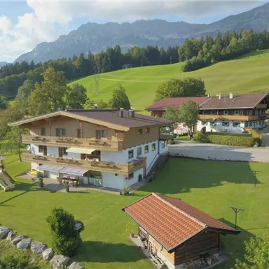 Ein schönes Gebäude in ländlicher Umgebung mit grünen Wiesen und Bergen im Hintergrund. Im Vordergrund befindet sich ein Spielplatz aus Holz.