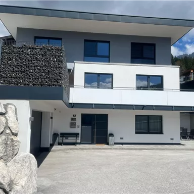 A modern house with multiple windows and a clear, bright design. The entrance is surrounded by a paved parking area.