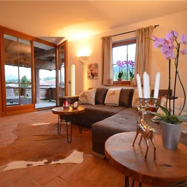Ein modernes Wohnzimmer mit einer bequemen Couch und Holztischen. Große Fenster lassen viel Licht herein und bieten einen Blick auf die Umgebung.