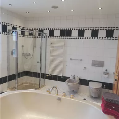 Ein modernes Badezimmer mit freistehender Badewanne und gläserner Dusche. Die Wände sind mit weißen Fliesen und schwarzen Akzenten gestaltet.