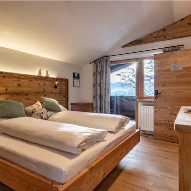 A cozy bedroom with wooden decor and a comfortable double bed. The large windows offer a view of the snowy landscape.