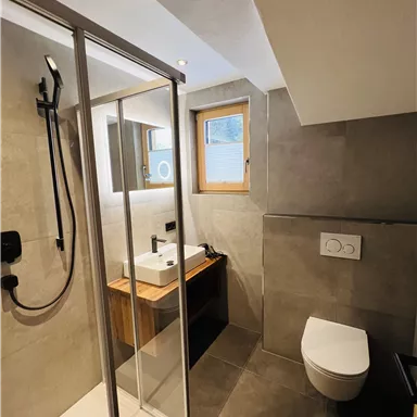 A modern bathroom with a shower, a sink, and a toilet. The walls are painted in neutral colors and there is a window for natural light.