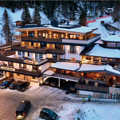 Ein stilvolles Hotel im Schnee, umgeben von Bäumen. Es gibt Parkplätze und einen schönen Blick auf die Skipisten.
