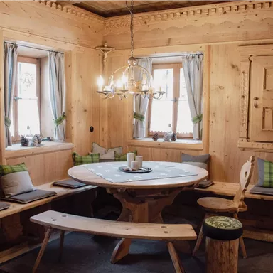 A cozy room with wooden paneling and a round table group. Benches and cushions invite you to linger.
